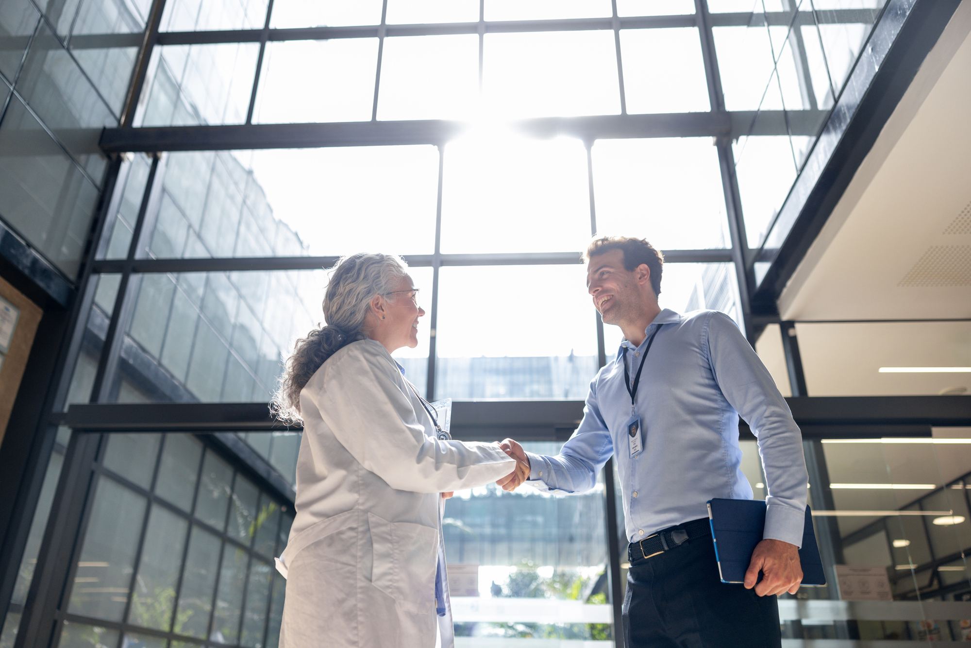 A physician and a business leader shaking hands in a bright atrium